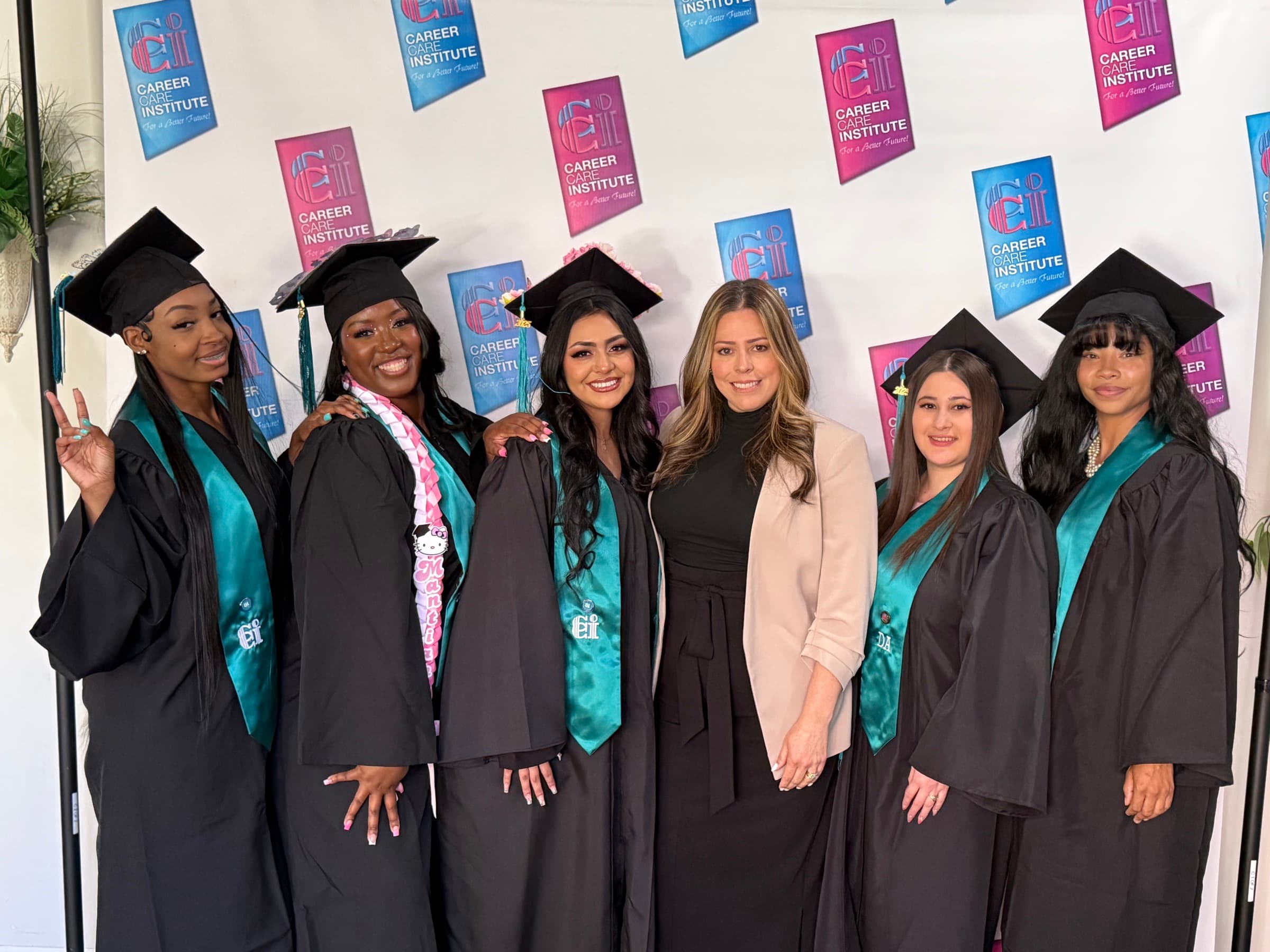 CCI graduates and a staff member posing together in front of a CCI backdrop.