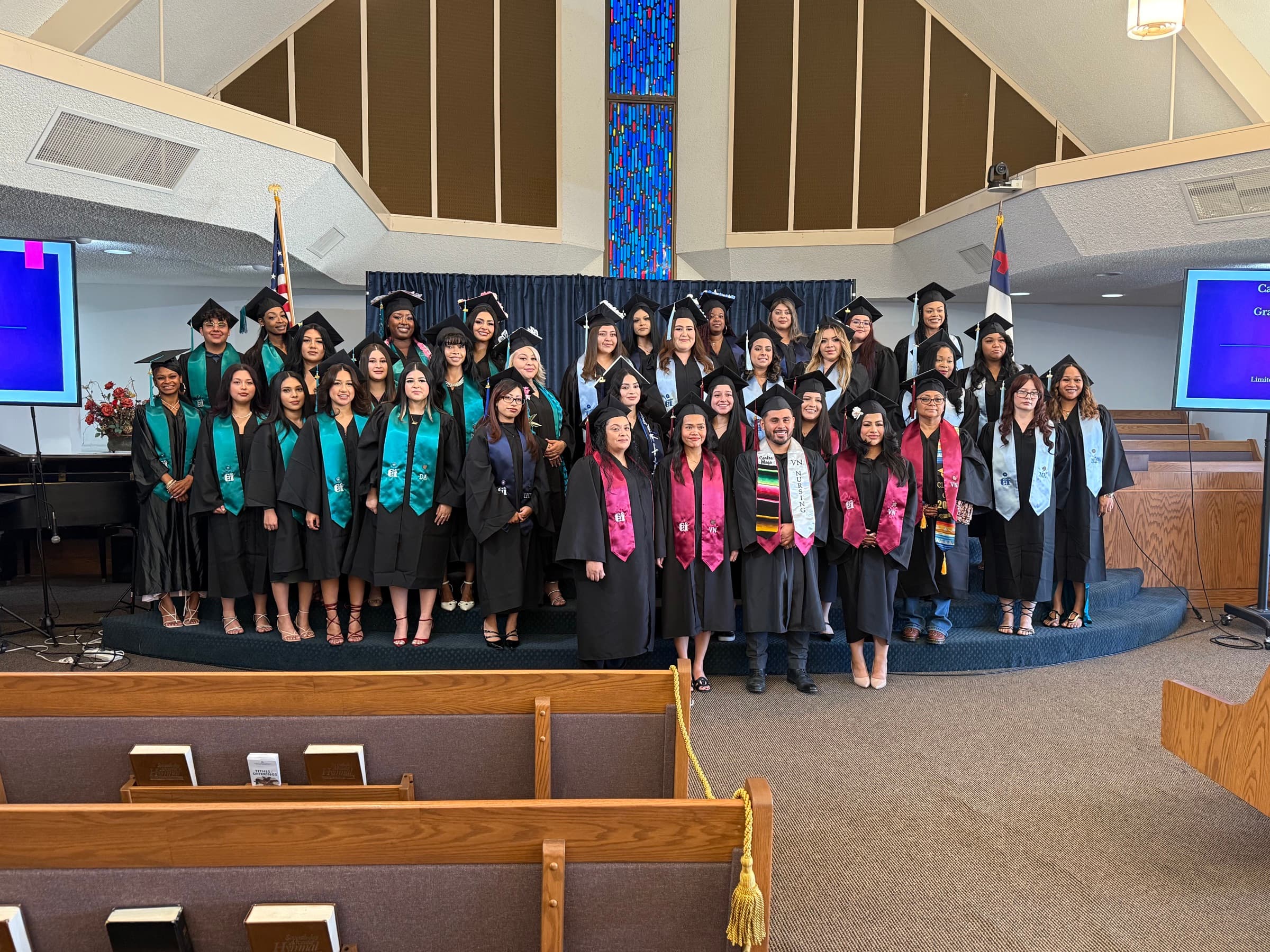 A large group of CCI graduates posing together in caps, gowns, and program stoles.