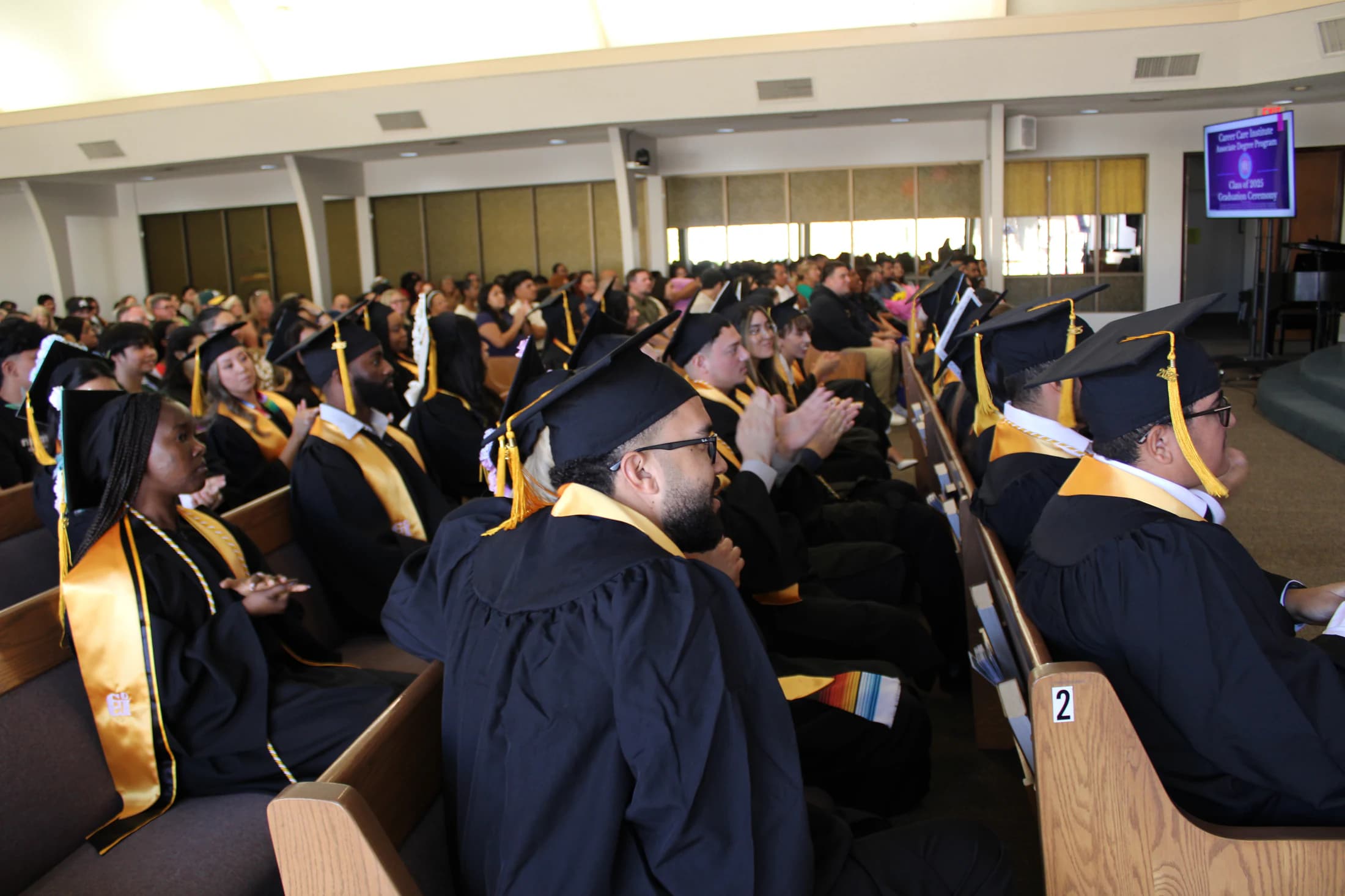 Career Care Institute graduates in caps and gowns sit during a graduation ceremony.
