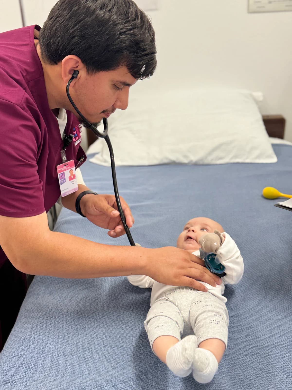 A Vocational Nursing student in burgundy scrubs practices an infant assessment with a stethoscope.
