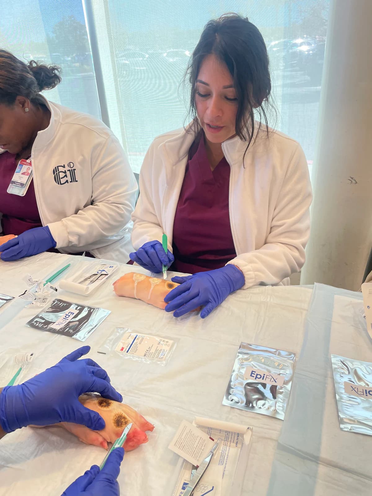 Vocational Nursing students in burgundy scrubs learn wound-care techniques during a hands-on training event.