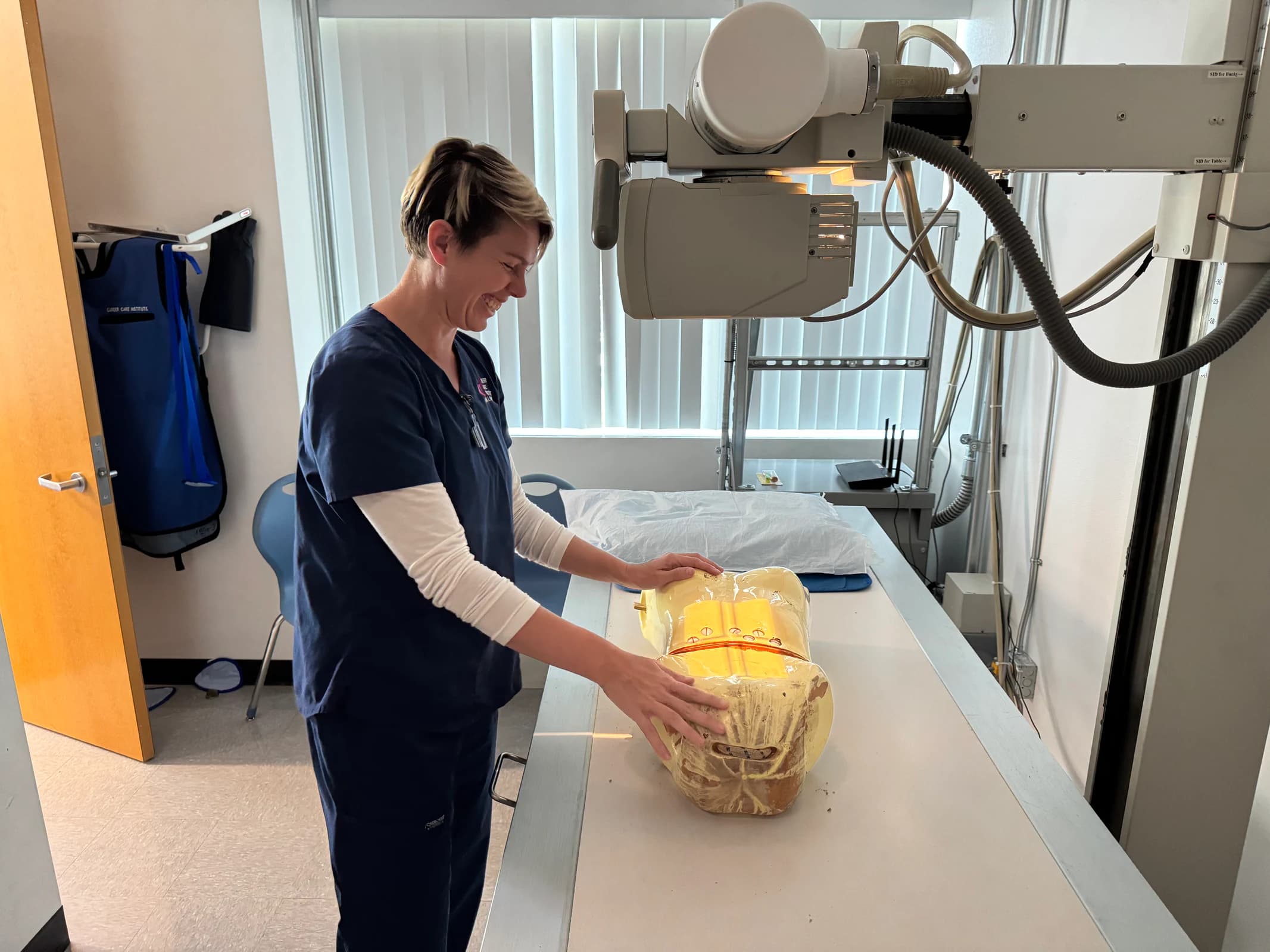 A person in CCI scrubs adjusts a torso mannequin beneath an X-ray unit.